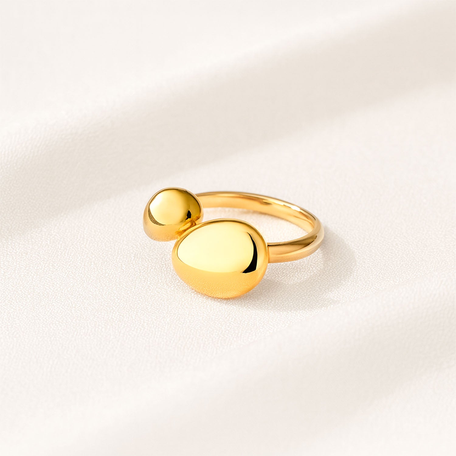 Gold ring with two round balls on a light beige background