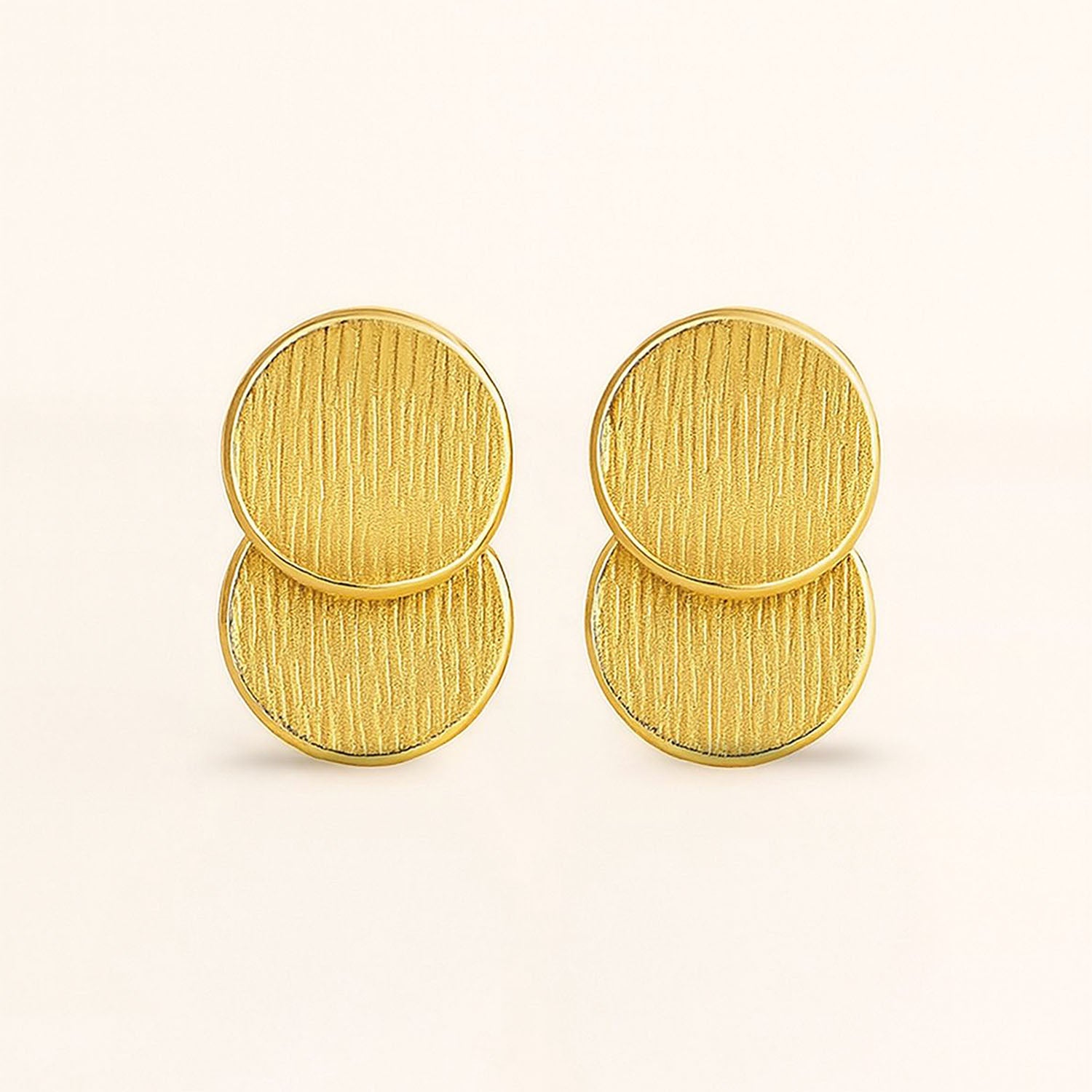 Pair of gold circular earrings on a light beige background